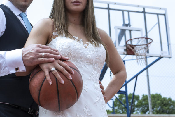 Love and Basketball Image. Woman in wedding dress standing next to groom holding a basketball.